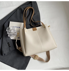 Detail of off-white tote bag with lychee texture, brown leather tag and wide shoulder strap