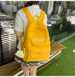 Dettaglio dello zaino in nylon giallo con ricamo bianco e ciondolo a forma di nuvola