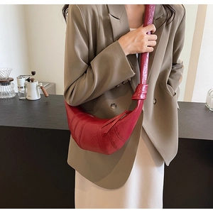 Detail of red crescent-shaped crossbody bag with soft pleats and knotted strap detail