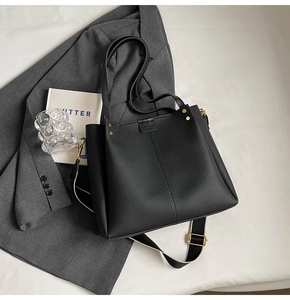 Detail of black lychee leather tote bag with wide canvas strap and gold metal rivets