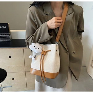 Detail of canvas bucket bag with brown leather trim and a plush cloud charm accessory