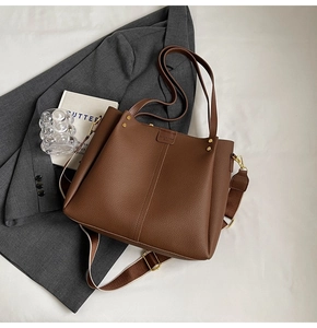 Detail of brown litchi pattern leather tote with wide woven strap and golden studs
