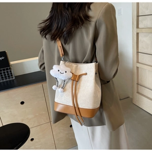 Detail of canvas bucket bag with leather base and plush cloud charm on a shoulder strap