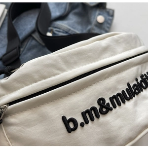 Nahaufnahme der weißen Canvas-Brusttasche mit schwarzer Stickerei und verstellbarem Gurt