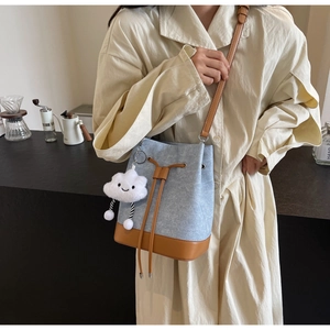 Detail of light blue textured fabric bucket bag with brown leather base and cloud charm