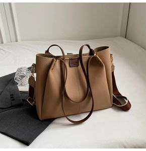 Detail of large beige leather tote bag with wide strap and gold hardware on soft background