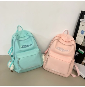 Dettaglio di zaini scolastici minimalisti in verde menta e rosa con ricamo e ciondolo peluche