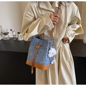 Detail of blue denim bucket bag with brown leather trim and white cloud charm