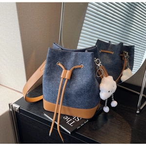 Detail of blue denim bucket bag with brown leather drawstring and cloud charm accessory