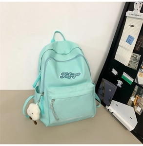Dettaglio dello zaino in tela verde menta con logo sulla tasca frontale e ciondolo peluche