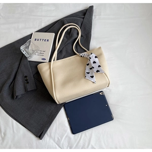 Detail of a cream tote bag with litchi texture and heart scarf in a professional desk setting