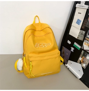 Dettaglio dello zaino in nylon giallo con ricamo bianco e decorazione a pompon