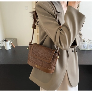 Détail d'un sac bandoulière marron foncé à texture tressée et lettrage doré chic