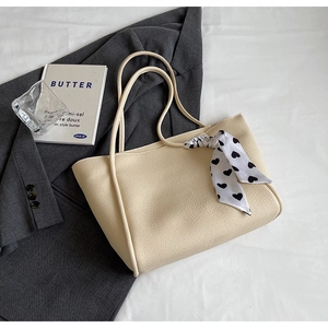 Detail of beige tote bag with lychee pattern leather and heart print scarf handle