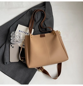 Flat lay of large khaki tote bag with wide strap on grey suit in a professional setting