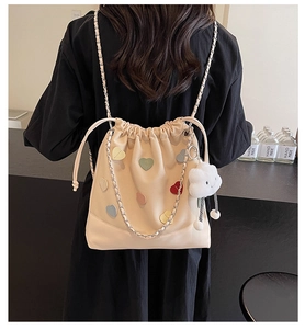 Detail of cream drawstring bucket bag with colorful heart patches and chain strap
