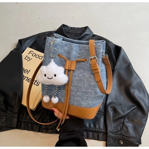 Detail of blue denim bucket bag with brown leather trim and a white cloud charm