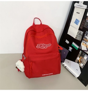 Dettaglio dello zaino in nylon rosso con ricamo bianco e ciondolo a pecorella