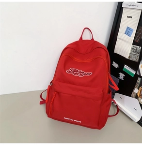 Dettaglio dello zaino rosso minimalista con tasca frontale e porta borraccia laterale