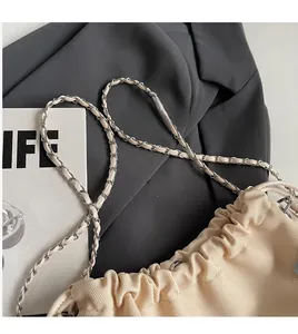 Detailed shot of cream drawstring bucket bag with silver metal chain and woven fabric texture