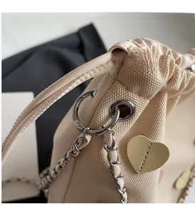 Detail of beige drawstring bucket bag featuring heart leather patch and silver metal chain