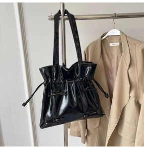 Detail of black patent leather tote bag with drawstring folds and ribbon bow accents