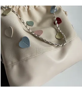 Close-up of canvas bucket bag with colorful leather heart patches and metal chain strap