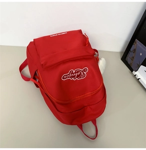 Dettaglio dello zaino rosso con logo ricamato e accessorio di peluche sul lato