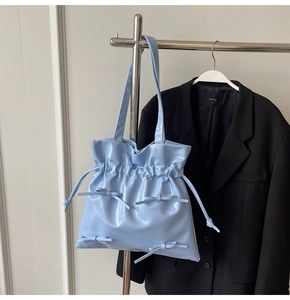 Detail of light blue patent leather tote bag with ribbon bows and drawstring texture