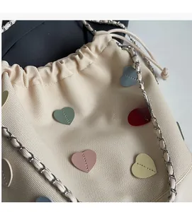 Detail of beige canvas bucket bag with colorful leather hearts and chain strap