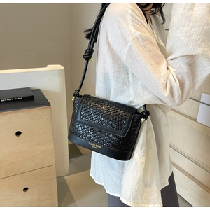Détail du sac bandoulière noir en cuir tressé avec logo doré et bandoulière à nœud
