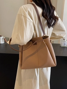 Large beige leather tote bag with wide shoulder strap shown on a model for daily commute