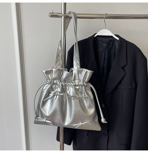 Detail of silver metallic drawstring tote bag with small bows on black blazer backdrop