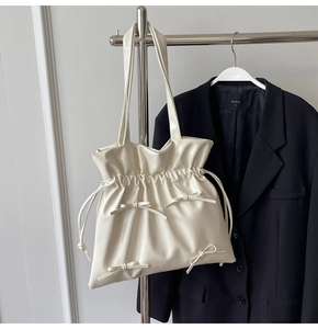 Close-up of white drawstring tote bag with decorative bows and thin shoulder straps