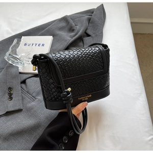 Détail d'un sac seau tressé noir avec bandoulière nouée et finitions dorées