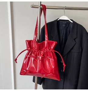 Detail of red glossy drawstring tote bag with elegant bows and pleated leather texture