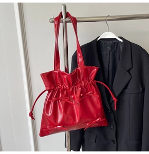 Detail of red drawstring tote bag with decorative bows on a black blazer backdrop