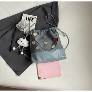 Detail of drawstring bucket bag featuring heart patches and chain strap with cloud charm