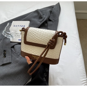 Détail du sac bandoulière en paille tissée avec bordure en cuir marron et logo lettrage