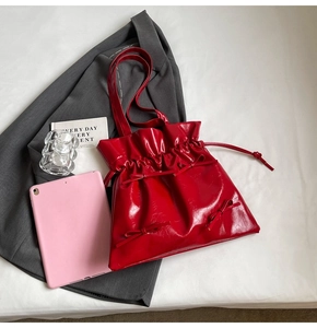 Detail of red glossy patent leather tote bag with drawstring folds and three bows