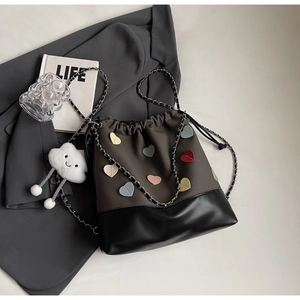 Detail of drawstring bucket bag featuring heart patches and a cloud plush charm