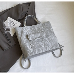 Détail du sac cabas argenté métallisé avec poche nœud et texture froissée sur lit