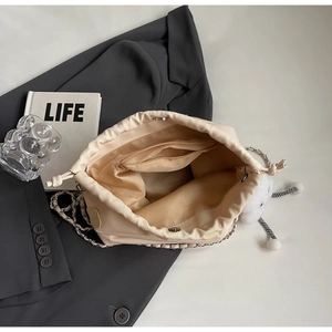 Close-up of cream drawstring bucket bag with silver chain strap and furry monster charm