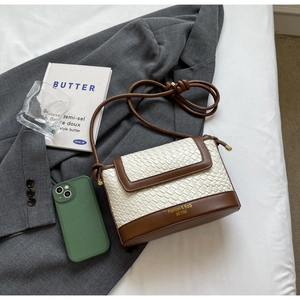 Détail d'un sac bandoulière en paille tressée avec bordure en cuir marron et logo