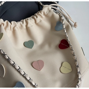 Detail of beige canvas bucket bag featuring colorful leather heart patches and chain strap