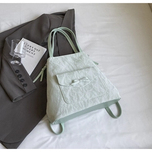 Détail du sac à dos vert menthe en tissu plissé avec nœud décoratif sur fond neutre