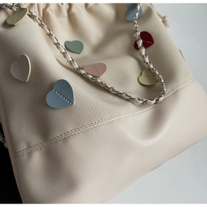 Detail of canvas bucket bag with colorful leather hearts and silver chain strap