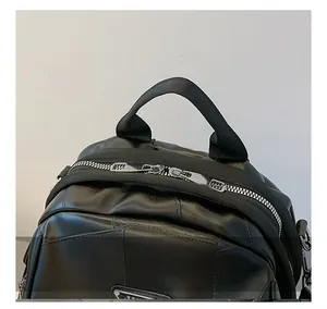 Close-up of black leather backpack featuring dual silver zippers and a top webbed handle