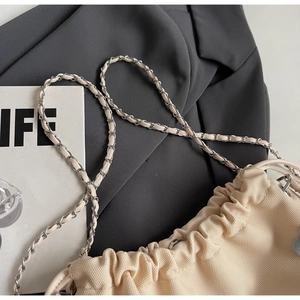 Close-up of the beige canvas texture and metal chain strap of the bucket bag