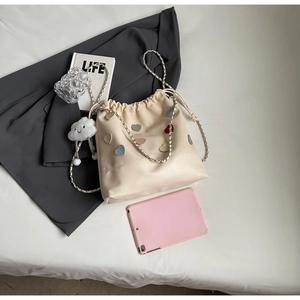 Close-up of beige drawstring bucket bag with colorful leather heart patches and metal chain